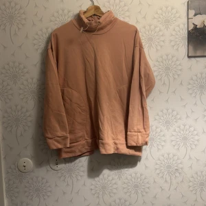 Rosa polotröja med omlott-detalj - Säljer en mysig rosa polotröja med unik omlott-detalj på baksidan. Tröjan har långa ärmar och en avslappnad passform, perfekt för kyliga dagar. Den är både stilren och bekväm.