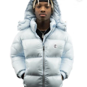 Lukamachain baby-blue puffjacket - Säljer en helt ny och superfin baby blå pufferjacka med huva från lukamachain. Jackan har en cool logga på bröstet och en stor stjärndetalj på ryggen. Jackan är perfekt för vintern och är även vattentät! Nypris-1873 kr