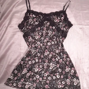 Blommig linne med spetsdetaljer - *Japanska märker*.                                                      Säljer ett supersött blommigt linne med smala axelband och spetsdetaljer. Linnet har en mörk bas med rosa och vita blommor, perfekt för sommardagar. 