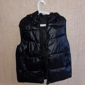 Svart dunväst med dragkedja - Snygg svart dunväst med dragkedja och huva. 