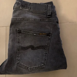 Mörk grå jeans från Nudie Jeans - Snygga  mörk gråa  jeans från Nudie Jeans med en klassisk femficksdesign. De har en diskret tvättad look och en knappgylf. Perfekta för en stilren och avslappnad stil.