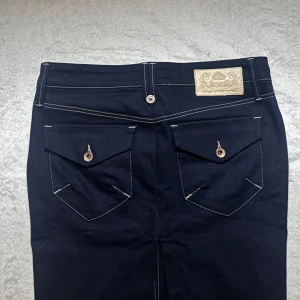 Blå jeanskjol från Fornarnia  - Snygg blå jeanskjol från fornarnia med kontrasterande sömmar och två bakfickor med knappar. Jeanskjolen har en superfin slits på baksidan. Midjemåttet är 76 cm.  Kjolen har en klassisk design med en knapp och dragkedja framtill. Perfekt för en stilren look. Storlek S. Aldrig använd super bra skick. 