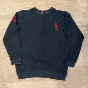 Polo Ralph Lauren tröja - Säljer en snygg mörkblå tröja från Polo Ralph Lauren med röd broderad logga på bröstet och siffran 3 på ärmen. Tröjan har långa ärmar och ribbade muddar vid ärmslut och nederkant. Och storlek 13 - 14 år. Perfekt för en stilren look!