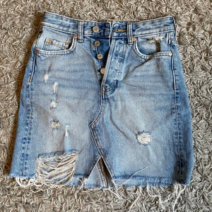 Blå jeanskjol från &Denim - Säljer en cool blå jeanskjol från &Denim i storlek 32. Kjolen har en sliten look med fransiga kanter och slitningar fram och bak. Sällan använd. 100kr