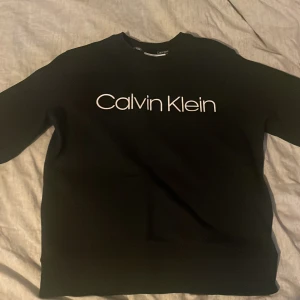 Svart tröja från Calvin Klein - Säljer en stilren svart tröja från Calvin Klein med deras ikoniska logga tryckt på framsidan. Perfekt för en avslappnad och trendig look.