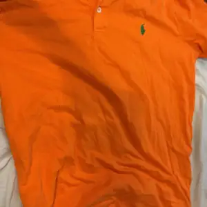 Säljer en snygg orange pikétröja från Ralph Lauren i storlek L. Tröjan är i Pima stretch mesh-material och har en klassisk krage med knappar. Perfekt för en stilren look. 🧡