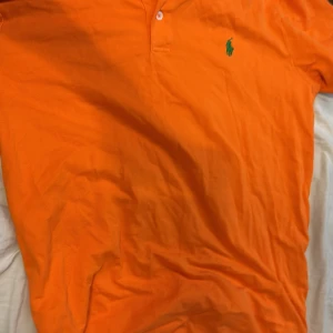 Orange pikétröja från Ralph Lauren - Säljer en snygg orange pikétröja från Ralph Lauren i storlek L. Tröjan är i Pima stretch mesh-material och har en klassisk krage med knappar. Perfekt för en stilren look. 🧡