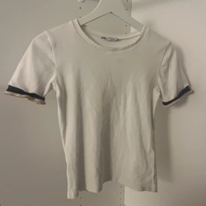 Vit T-shirt - Säljer en vit T-shirt från Zara med detaljer längst ut på ”armarna”. Sparsamt använd och inga defekter.