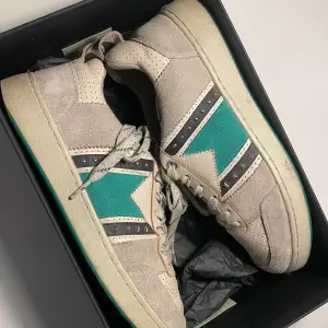 Säljer ett par snygga beige sneakers från Maje. De har en cool design med gröna och svarta detaljer samt nitar. Skorna är i mocka och har snörning framtill. Använda men inga rejäla skador, behöver rengöras. Pris kan diskuteras! 