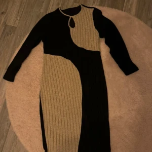 Svart och beige långärmad klänning - Säljer en unik svart och beige klänning med långärmad design. Klänningen har ett coolt asymmetriskt mönster och en liten öppning vid halsen som ger en extra detalj. Perfekt för höst och vinter!