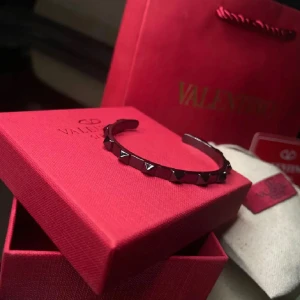 Svart armband med nitar från Valentino - Säljer ett snyggt armband från Valentino med coola nitar. Perfekt för att ge din outfit en edgy touch. Armbandet kommer i en lyxig röd förpackning med Valentino-loggan. Passar både till vardags och fest!