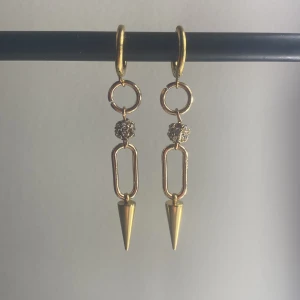 Ett par guldiga örhängen med en glittrig pärla i mitten - Det är ett par örhängen med en glittrig på i mitten