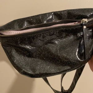 Svart glittrig axelväska med leopardmönstrat foder - Säljer en supercool svart glittrig axelväska med ett snyggt leopardmönstrat foder. Väskan har en dragkedja upptill och en justerbar rem. Perfekt för att ge din outfit lite extra bling! 🖤✨