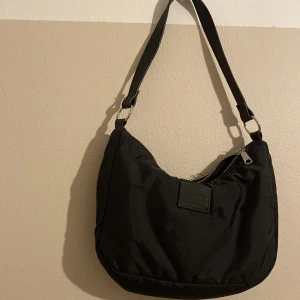 Svart axelväska från Divided Supply - Säljer en snygg svart axelväska från Divided Supply. Väskan är i syntetmaterial och har en praktisk dragkedja upptill. Perfekt för vardagsbruk och passar till de flesta outfits. Den har en justerbar axelrem för extra komfort. Nästan aldrig använd!😍