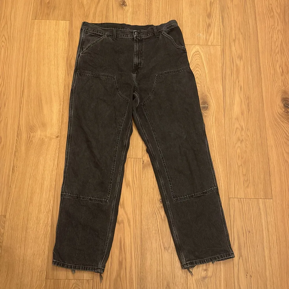 Säljer ett par svarta byxor från Carhartt. De har en robust design med förstärkta knän och en avslappnad passform. Perfekta för både arbete och vardag. Byxorna har en klassisk femficksdesign och en dragkedja i gylfen. . Farkut & Housut.