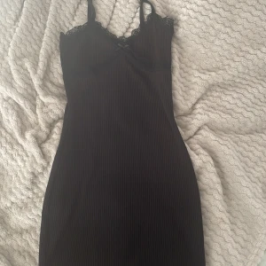 Svart tight klänning - Tight svart klänning med en liten rosett och spets. Använd ett par fåtal gånger och säljer då den inte används längre.