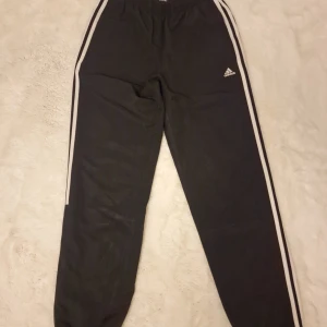 Svarta mjukisbyxor från Adidas - Säljer ett par svarta byxor från Adidas. De har de klassiska tre ränderna längs sidorna och en liten Adidas-logga på benet. Byxorna är i storlek S och är perfekta för träning eller en chill dag. De är gjorda i ett mjukt och bekvämt material.