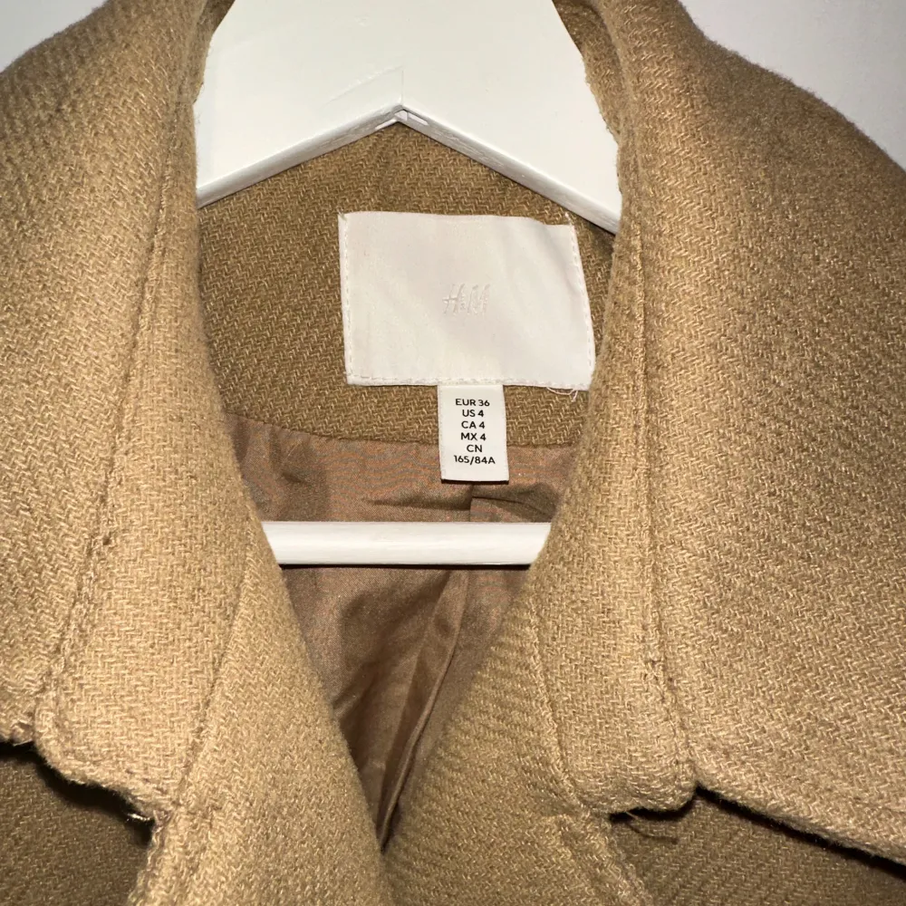 Säljer en snygg beige kappa från H&M i storlek 36. Den har en klassisk design med ett bälte i midjan för en elegant passform. Perfekt för höst och vår även under vintern! . Jackor.