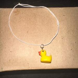 Armband med gul anka - Säljer ett supergulligt armband med en liten gul anka som hänge. Ankan är gjord av plast och har en söt orange näbb. Perfekt för att lägga till en rolig touch till din outfit!