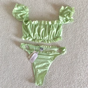 NA-KD ljusgrön bikini med volanger - Bikini från NA-KD med volanger. Överdelen är i storlek S och underdelen I XS men passar bättre på en S då den är ganska stor. Ny med prislappar men råkat försvinna på överdelen.