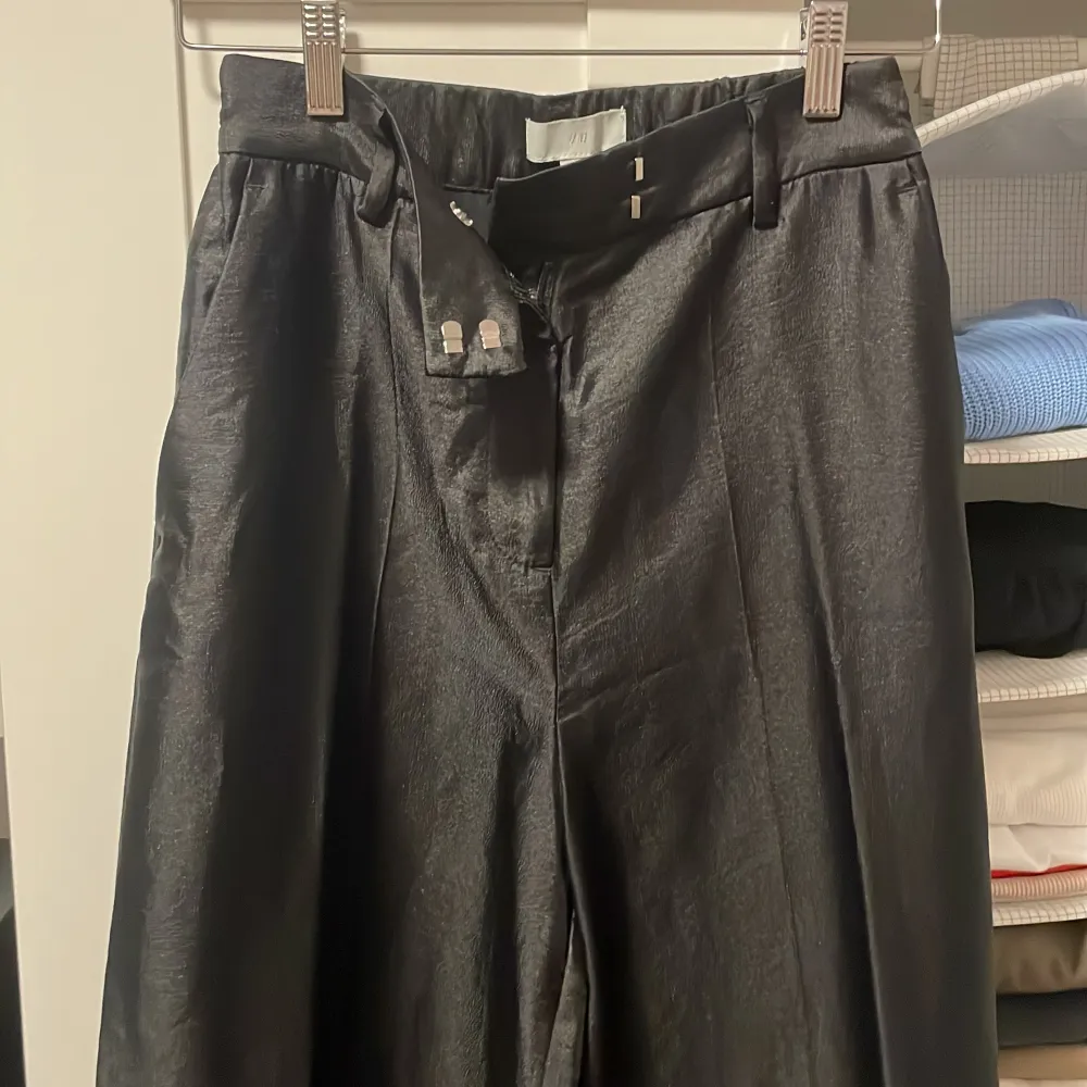 Säljer ett par eleganta svarta byxor från H&M i storlek 36. De är högmidjade och har en vid passform som ger en snygg siluett. Materialet ser ut att vara en glansig polyester, vilket ger en lyxig känsla. Perfekta för både fest och vardag!. Jeans & Byxor.