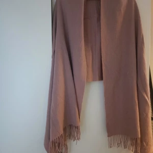 Rosa halsduk från Stockh LM - Säljer en superfin rosa stor sjal från Stockh LM. Den är riktigt mjuk och har fransar i ändarna som ger en snygg touch. Perfekt för att hålla sig varm och stilig under kyliga dagar. Passar till både vardag och fest! Ylle. 