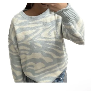 Ljusblå och vit mönstrad tröja - Säljer en supermysig ljusblå och vit tröja med ett coolt zebramönster. Tröjan är långärmad och perfekt för kyliga dagar. Den har en normal passform och är gjord i ett mjukt material som känns skönt mot huden. Perfekt för både vardag och mysiga hemmakvällar! använd sällan därav sälj, osäker på storlek men tippar någonstans mellan XS/S
