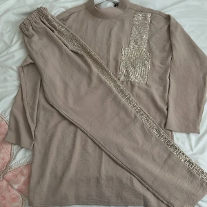 Beige tröja med paljettdetaljer - Säljer en snygg beige tröja med glittriga paljettdetaljer. Tröjan har en hög krage och trekvartsärmar, vilket gör den perfekt för både vardag och fest. Paljetterna ger en extra touch av glamour. Perfekt för dig som vill sticka ut lite extra! ✨