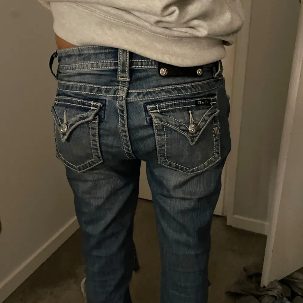 MISS ME blå jeans med coola slitningar på knäna. låg midja och en bootcut passform. Jeansen har snygga detaljer med knappar och fickor bak.midje mått ca : 40 men strechiga. innerbenslängd: ca 79. igensytt hål vid skrevet som inte syns alls. Jeans & Byxor.