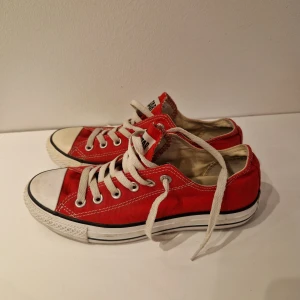 Röda Converse All Star sneakers - Säljer ett par klassiska röda Converse All Star sneakers. De har en låg modell med vita snören och en vit gummisula. Skorna är i bra skick och perfekta för både vardag och fest. Passar till nästan alla outfits!