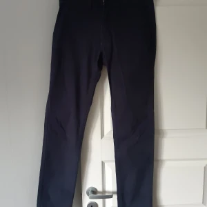 Svarta stretchchinos från 157 - Säljer ett par marinblåa stretch chinos från 157 i storlek small. De är bekväma och stilrena, perfekta för både vardag och lite mer uppklädda tillfällen. Byxorna har en snygg detalj vid bakfickan och är använda endast en gång.