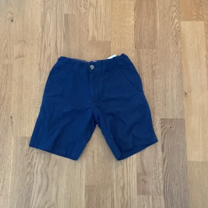 Mörkblå shorts från 157 - Säljer ett par mörkblå shorts från 157 i storlek 140. De är perfekta för sommaren med en bekväm passform och elastisk midja. Shortsen har en knapp och dragkedja framtill samt fickor på sidorna. Perfekta för både lek och vardag!