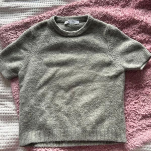 Grå stickad tröja från H&M - Säljer en mysig grå stickad tröja från zara. Den har korta ärmar och en rund halsringning. Perfekt för kyliga dagar när du vill vara både bekväm och stilren. Passar bra till både jeans och kjol!