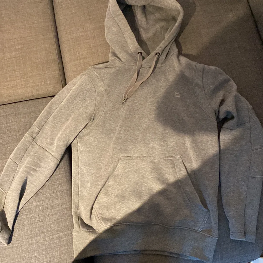 Säljer en stilren och bekväm grå hoodie från ARW. Den har en klassisk design med en stor ficka framtill och en justerbar huva. Perfekt för både vardag och chill. Passar bra till jeans eller mjukisbyxor! Armbågarna är lite slitna men man ser det knappt och hoodien är jätte snygg och varm👍. Tröjor & Koftor.