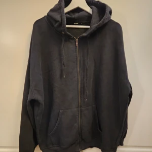 Svart hoodie med dragkedja - Säljer en använd svart hoodie med dragkedja. Den är perfekt för kyliga dagar och har en skön, avslappnad passform. Hoodien har en stor huva och praktiska fickor framtill. Perfekt för både vardag och mysiga hemmakvällar. Mer som strl L