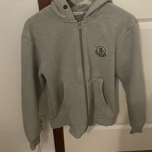 Grå fleecejacka från Moncler - Säljer en supermjuk och varm grå fleecejacka från Moncler. Taggen fungerar men jag vet inte om den är äkta. Har en defekt vid ena sidan av fickan - se sista bilden och en liten fläck men det är på insidan av koftan. Pris kan diskuteras 