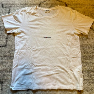 Saint Laurent t-shirt - Säljer denna snygga och trendiga Saint Laurent t-shirten. T-shirten är i storlek L men passar M-S. Passar dig perfekt som är runt 175-180cm och väger runt 65kg. Skick 9/10.  !OBS! Defekt förekommer, deofläckar. Nypris runt 5000kr. 