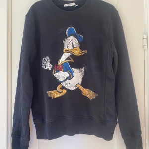 Svart sweatshirt med Kalle Anka Disney signature från Emilio i strl S - Svart sweatshirt med Kalle Anka Disney signature från Emilio i strl S.  Använd men i fint begagnat skick.  Mått Över bröstet: ca 51 cm Längd från axeln och ner: ca 63 cm  100% bomull   Kommer från ett djur och rökfritt hem.