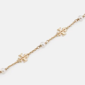 Guldarmband med pärlor och dekorativa detaljer - Säljer ett tory burch guldarmband med vita pärlor. Armbandet har en fin kedja med små guldfärgade symboler som ger en lyxig känsla. Perfekt för både vardag och fest! Den är använd så färgen har gått bort litegrann. Ej äkta 