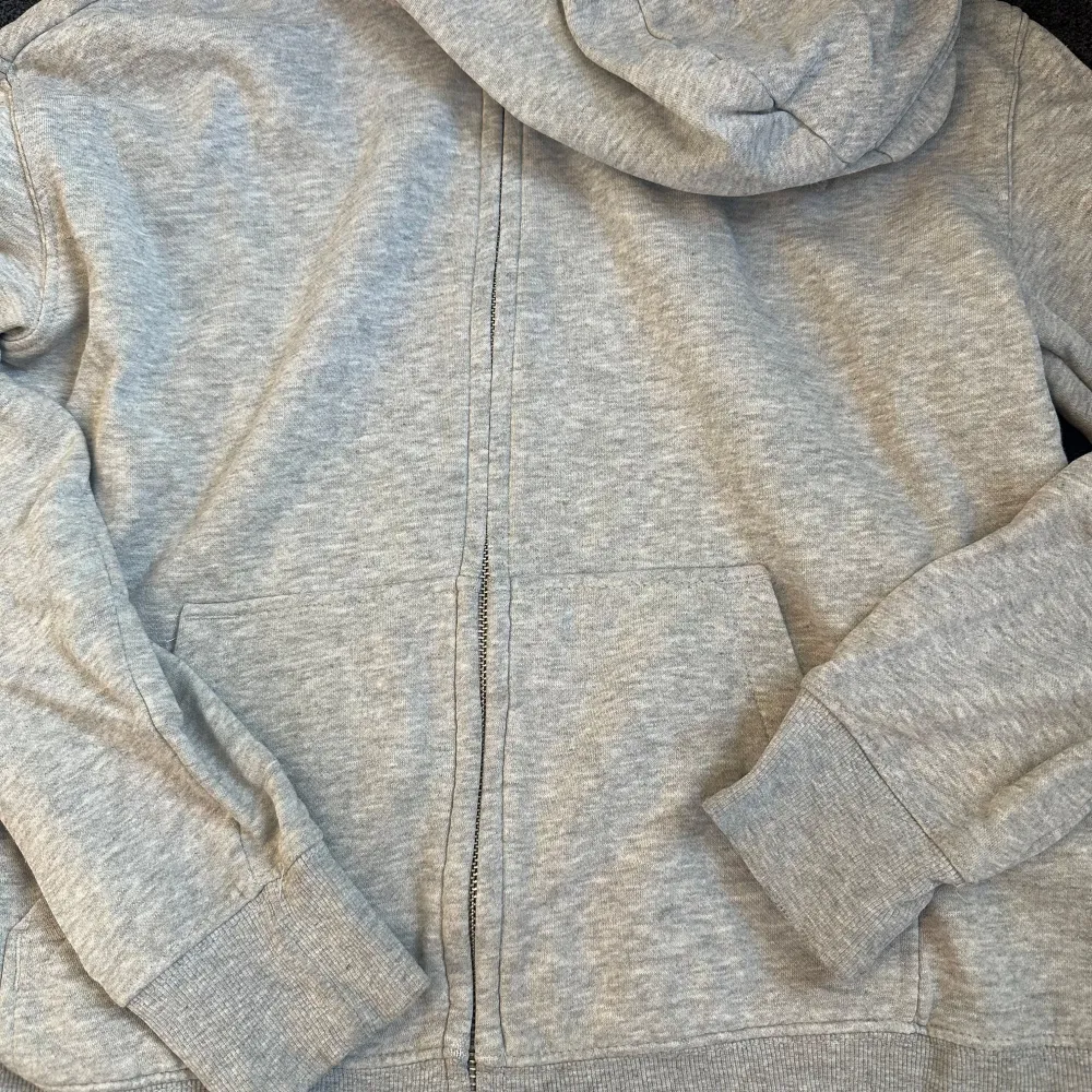 Säljer en grå hoodie. Den är supermjuk och perfekt för kyliga dagar. Hoodien har en dragkedja framtill och fickor på magen. Den har långa ärmar och en justerbar huva med snören. Perfekt för en avslappnad stil!. Tröjor & Koftor.