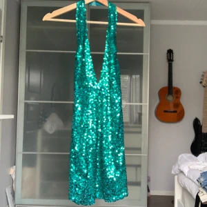 Grön glittrig klänning från Oneness - Säljer en superfin grön glittrig klänning från Oneness. Den har en djup v-ringning och är perfekt för festliga tillfällen. Klänningen är ärmlös och har en tight passform som verkligen framhäver figuren. Perfekt för nyår eller en glittrig utekväll! ✨