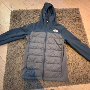 Vår jacka/fleecemed luva/ cardigan - Säljer en snygg blå jacka från The North Face i storlek L i ungdom. Motsvarar ungefär stolek 150. Jackan har en dragkedja framtill och en praktisk huva. Perfekt för hösten /våren. Den är i nyskick. 