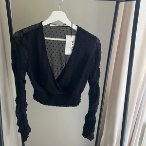 Svart topp - Svart topp från NAKD. Genomskinligt material med prickar, ”swiss” detaljer i armarna. Aldrig använd. 