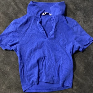 Marinblå ribbad pikétröja  - Säljer en snygg blå ribbad pikétröja från Ner yorker. Tröjan har korta ärmar och en klassisk krage med knappar. Perfekt för en avslappnad stil.