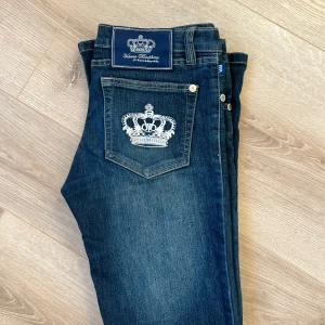 Mörkblå Victoria Beckham jeans - Snygga mörkblå R&R Victoria Beckham jeans med broderade kronor på bakfickorna. De har en låg midja och en bootcut-stil som ger en retro känsla. Perfekta för en avslappnad look med en touch av glamour.