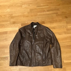 Brun skinnjacka från Lindbergh - Snygg brun skinnjacka från Lindbergh med dragkedja framtill och två bröstfickor med dragkedjor. Jackan har en stilren design och är perfekt för en cool look.