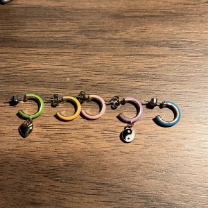 Färgglada örhängen med berlocker - Säljer ett set med fem färgglada örhängen i olika färger: grönt, orange, ljus rosa, lila och blått. Två av örhängena har berlocker, ett med ett hjärta och ett med yin-yang symbol. Perfekt för att mixa och matcha!