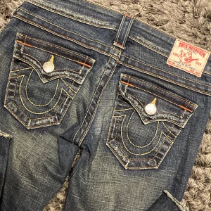 True Religion jeans  - Säljer ett par snygga blå jeans från True Religion med ikoniska bakfickor och kontrastsömmar. Jeansen har en lågmidjad passform och utsvängda där nere. Tillverkade i USA. De är klippta där nere. Skriv gärna ifall du har några frågor!❤️kan sänka priset så tveka inte att fråga❤️
