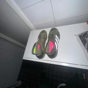 Adidas fotbollsskor i grönt och vitt - Snygga gröna Adidas fotbollsskor med vita ränder och färgglada detaljer på insidan. Perfekta för fotbollsplanen med en stilren design och bra passform.