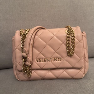 Ljusrosa Valentino axelväska  - Snygg ljus rosa axelväska från Valentino med quiltat mönster och guldfärgade kedjedetaljer. Väskan har en elegant design med logotyp framtill och en praktisk storlek för vardagsbruk. Priset går att diskuteras